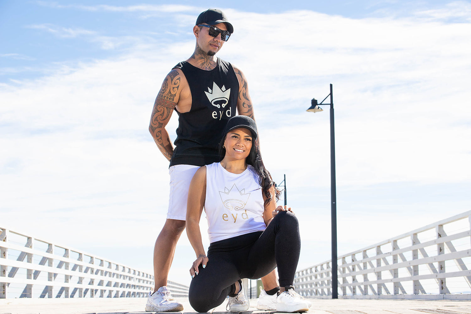 Photo of man standing and woman sitting wearing eyd unisex tank singlets